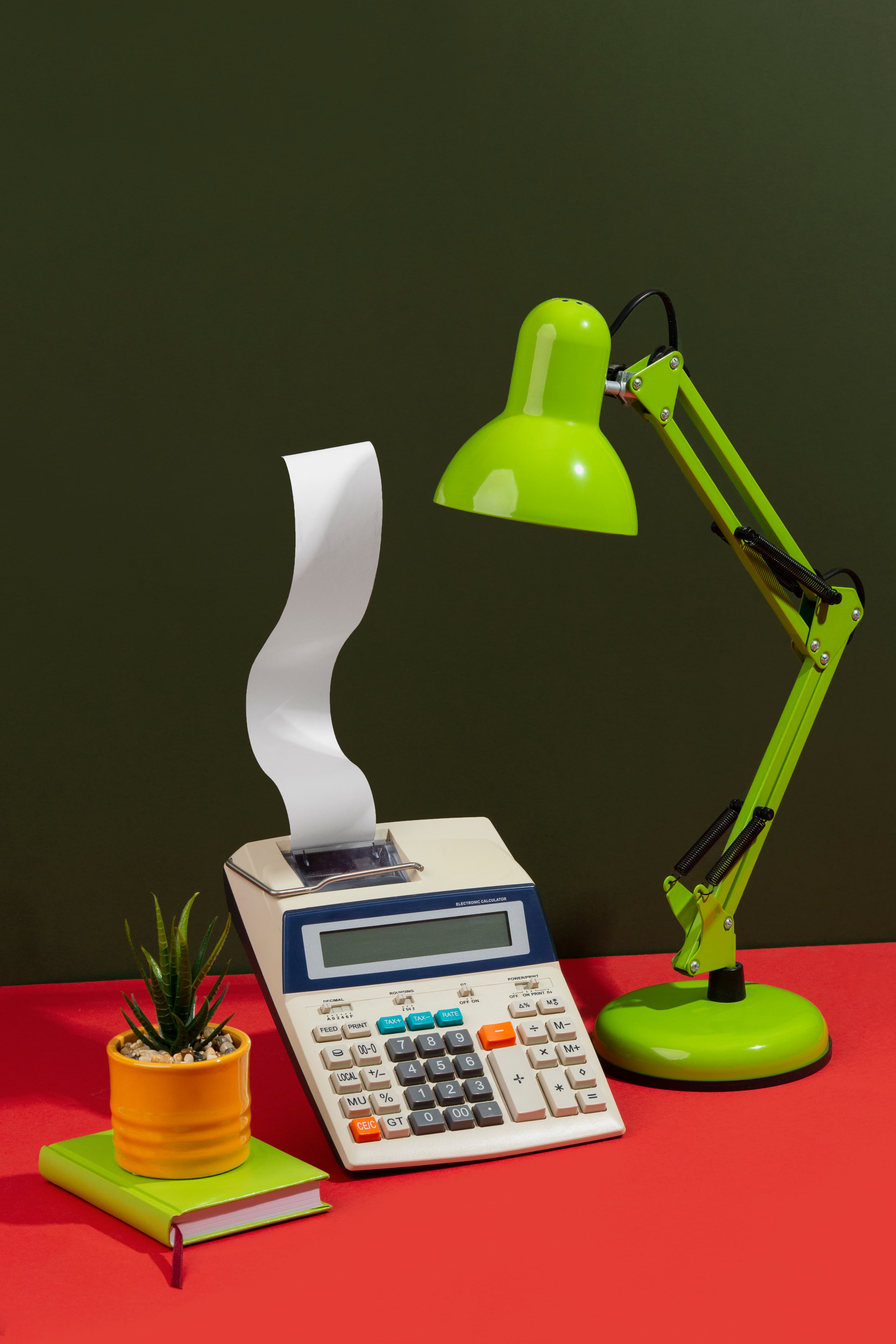 Vintage calculator with receipt roll beside a green desk lamp